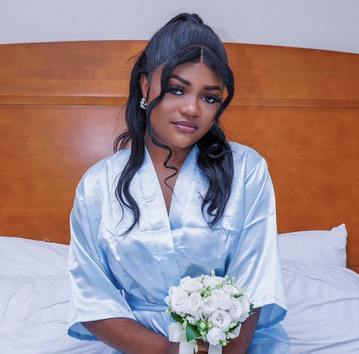 Bride getting ready in a satin robe holding a white rose bouquet