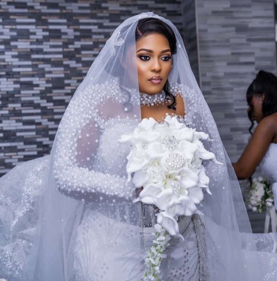 Bridal gown with pearl beading and cathedral veil, holding a white bouquet