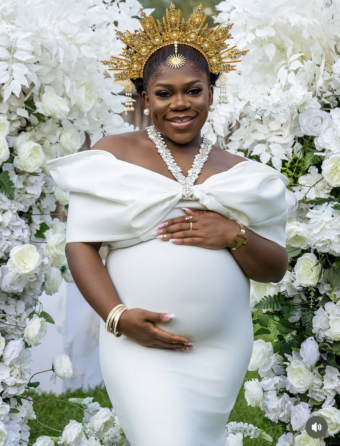 Maternity photoshoot with gold sunburst crown and white floral backdrop